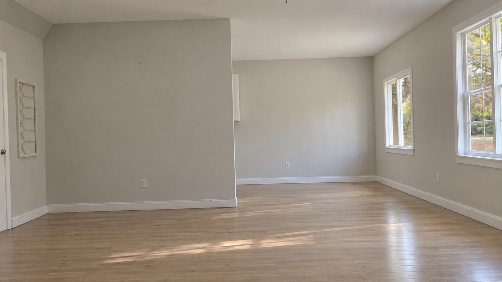 An empty living room with bare walls and wood floors, as photographed on a phone